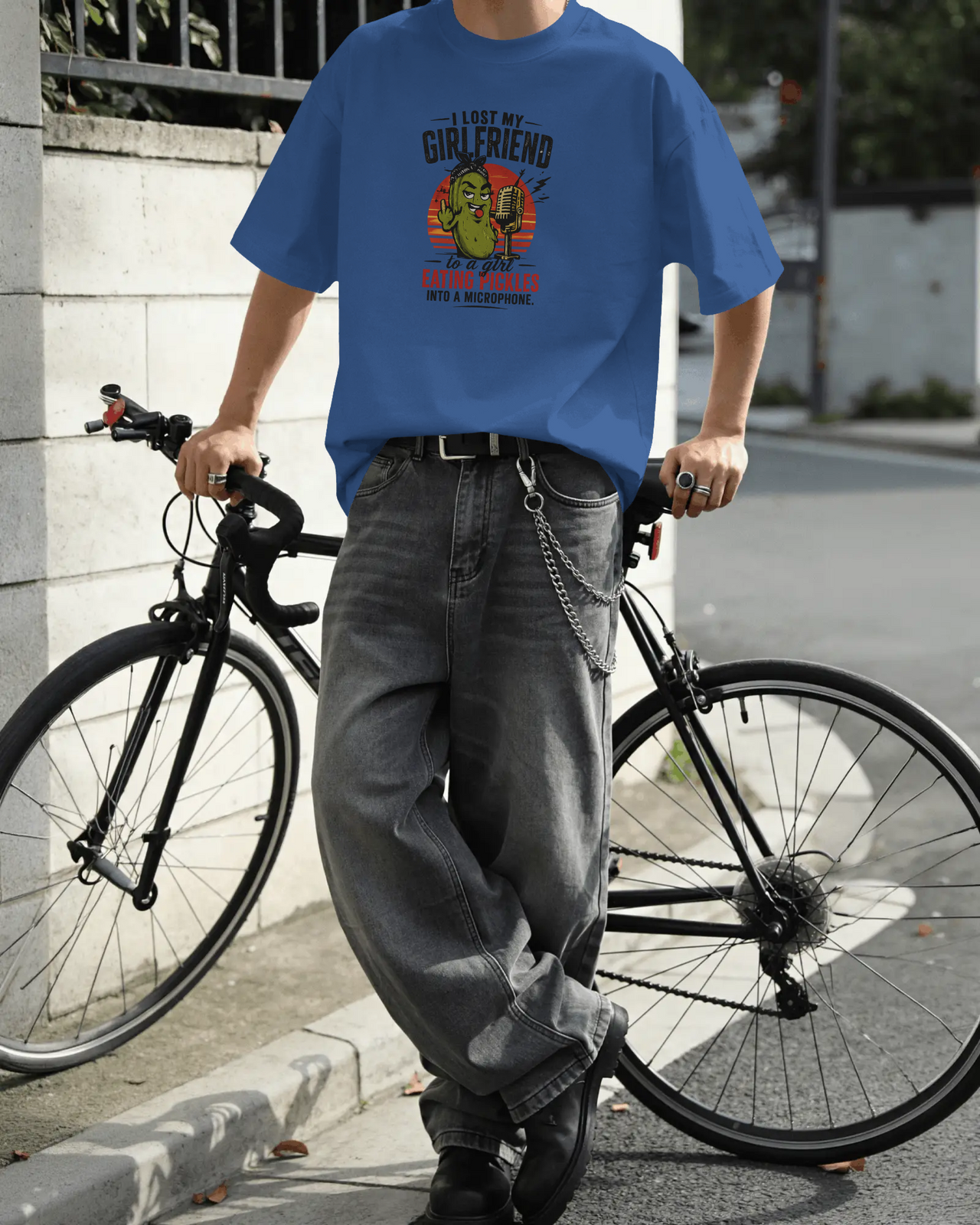 Person wearing a blue t-shirt with a graphic design, standing next to a bicycle on a street. ASMR Took My Girl - The Pickle Whisperer