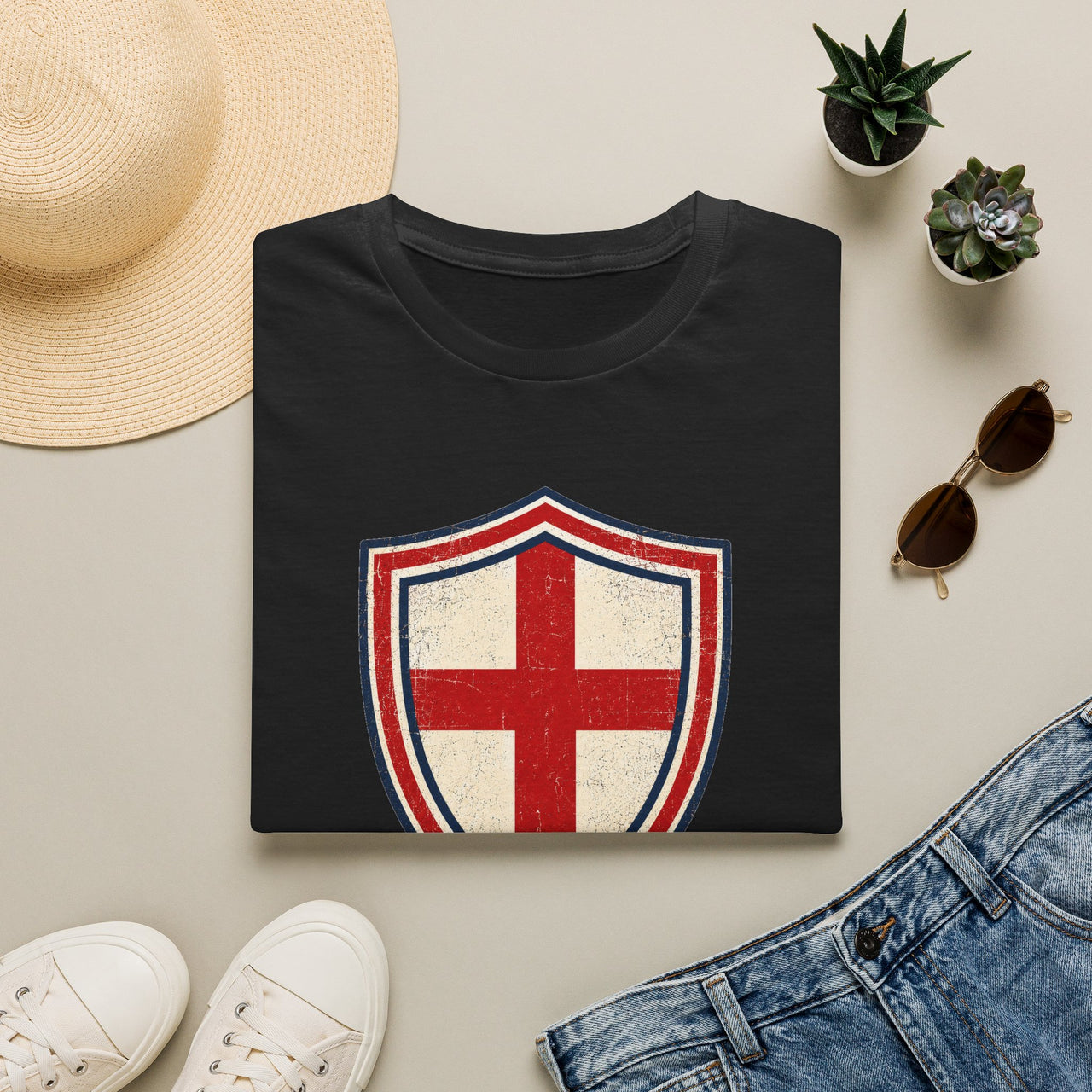 Black t-shirt with a red and white shield design on a light surface with accessories.