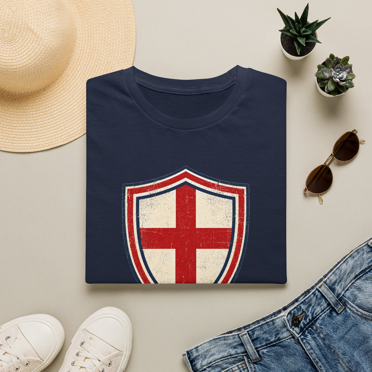 Navy blue t-shirt with a red and white shield design on a light surface with accessories.