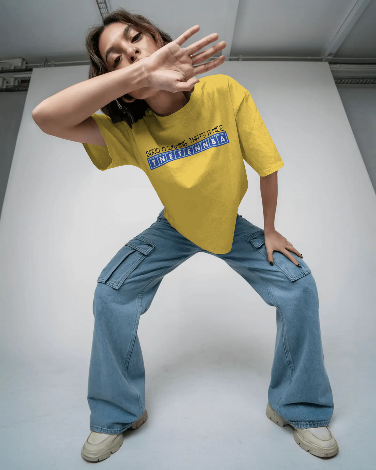 Person wearing a yellow t-shirt and blue jeans posing against a white  - Good Morning That’s A Nice TNETENNBA - The IT Crowd T-Shirtbackground