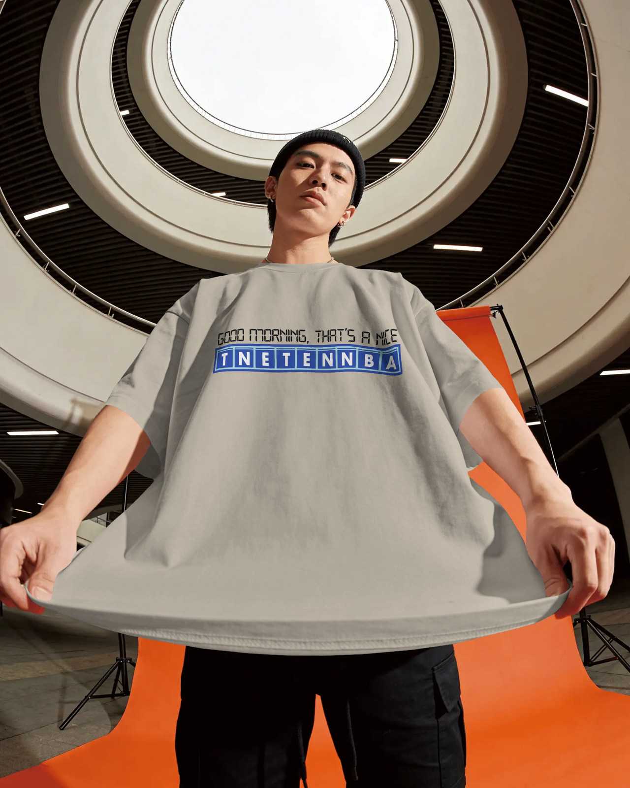 Person wearing a gray t-shirt with text in an indoor setting - Good Morning That’s A Nice TNETENNBA - The IT Crowd T-Shirt