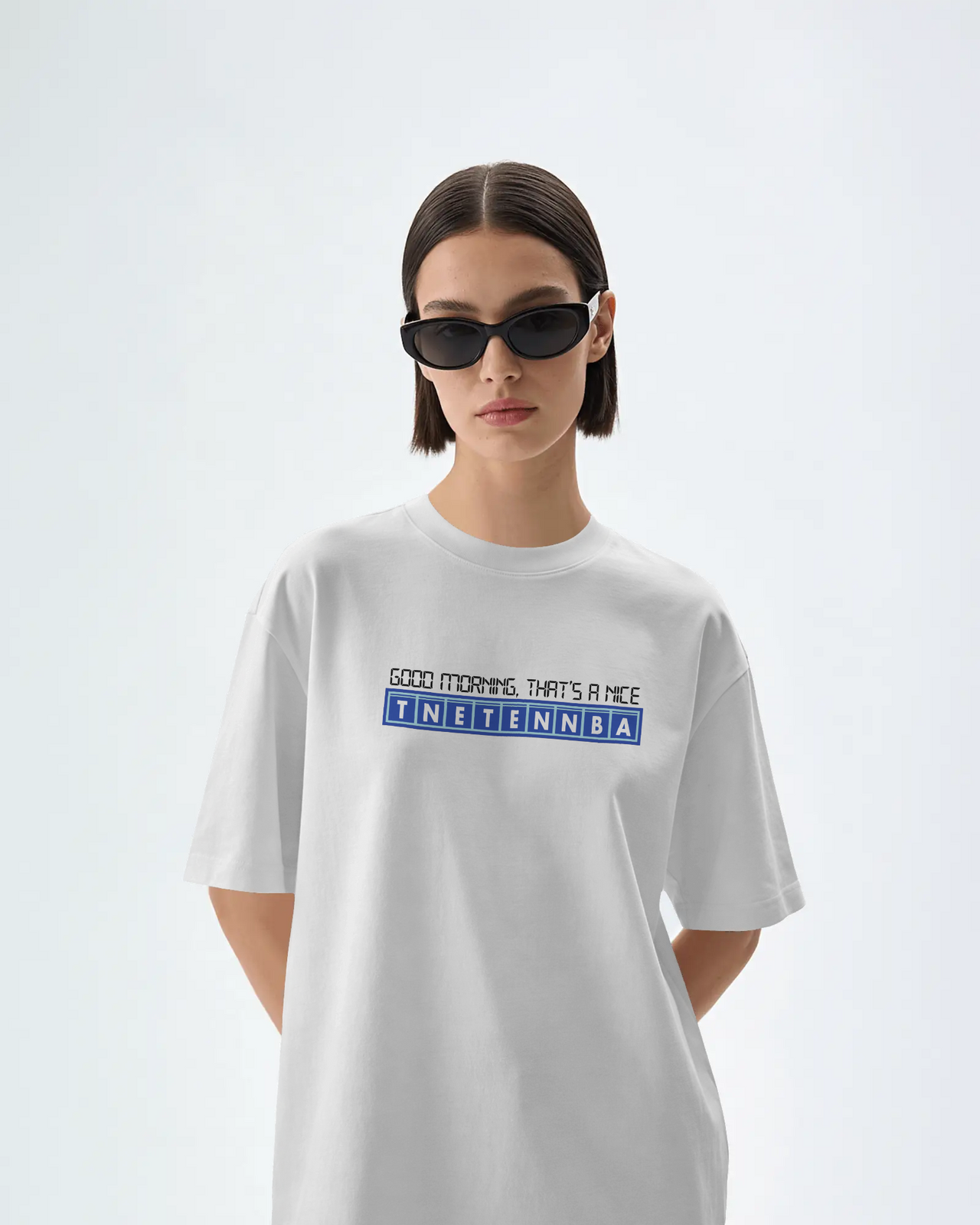 Person wearing a white t-shirt with text on a light gray background - Good Morning That’s A Nice TNETENNBA - The IT Crowd T-Shirt