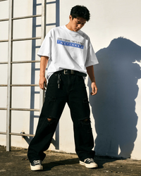 Thumbnail for Person wearing a white oversized t-shirt with text and black pants standing against a white wall with a metal ladder. - Good Morning That’s A Nice TNETENNBA - The IT Crowd T-Shirt