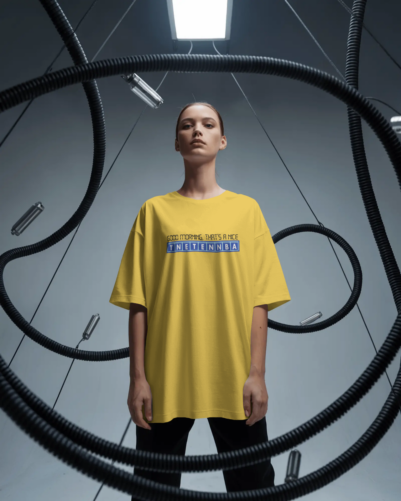 Person wearing a yellow t-shirt with text in a dark, industrial setting - IT Crowd - Tnetennba