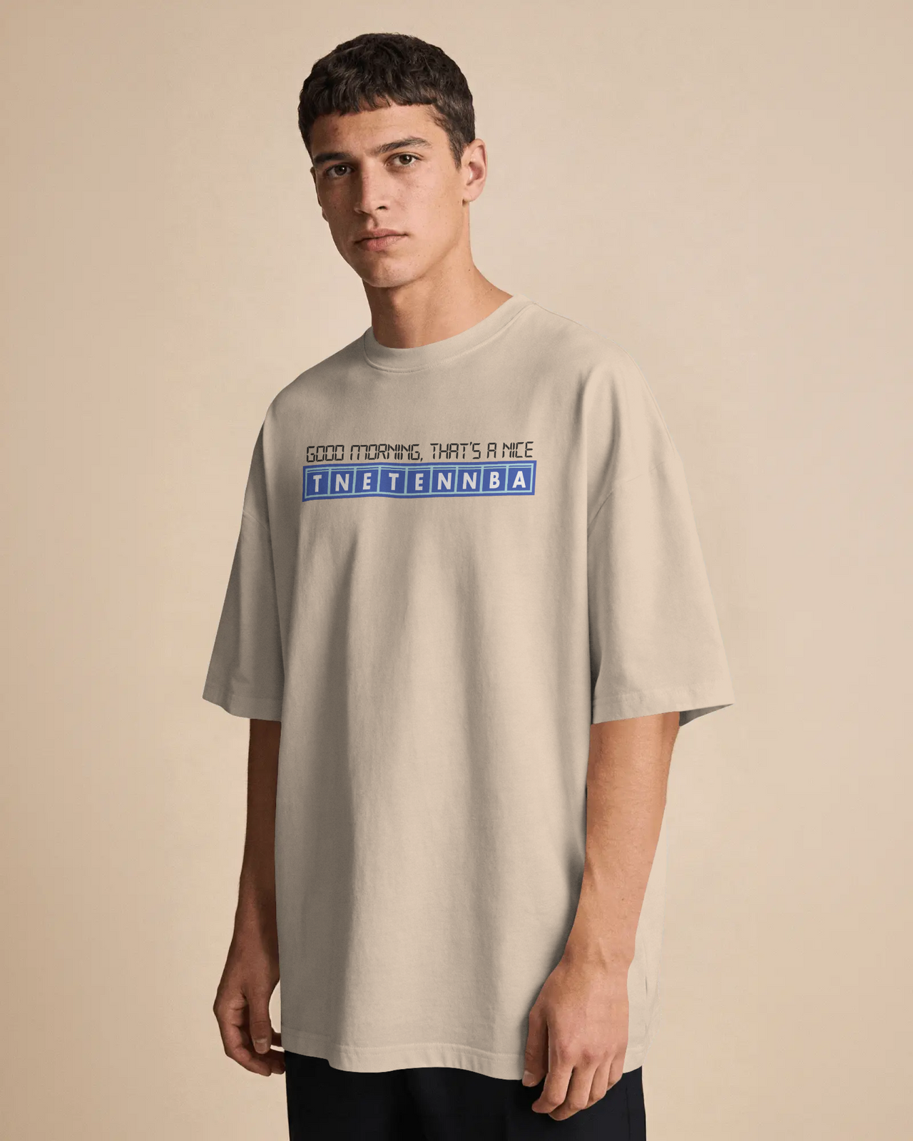 Man wearing a beige t-shirt with text on a beige background - Good Morning That’s A Nice TNETENNBA - The IT Crowd T-Shirt