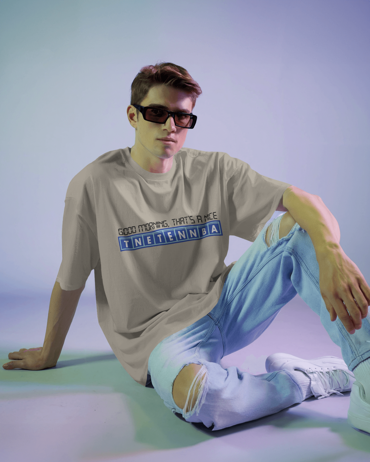 Person wearing a beige t-shirt with text and light blue jeans sitting on a gradient background - IT Crowd - Tnetennba