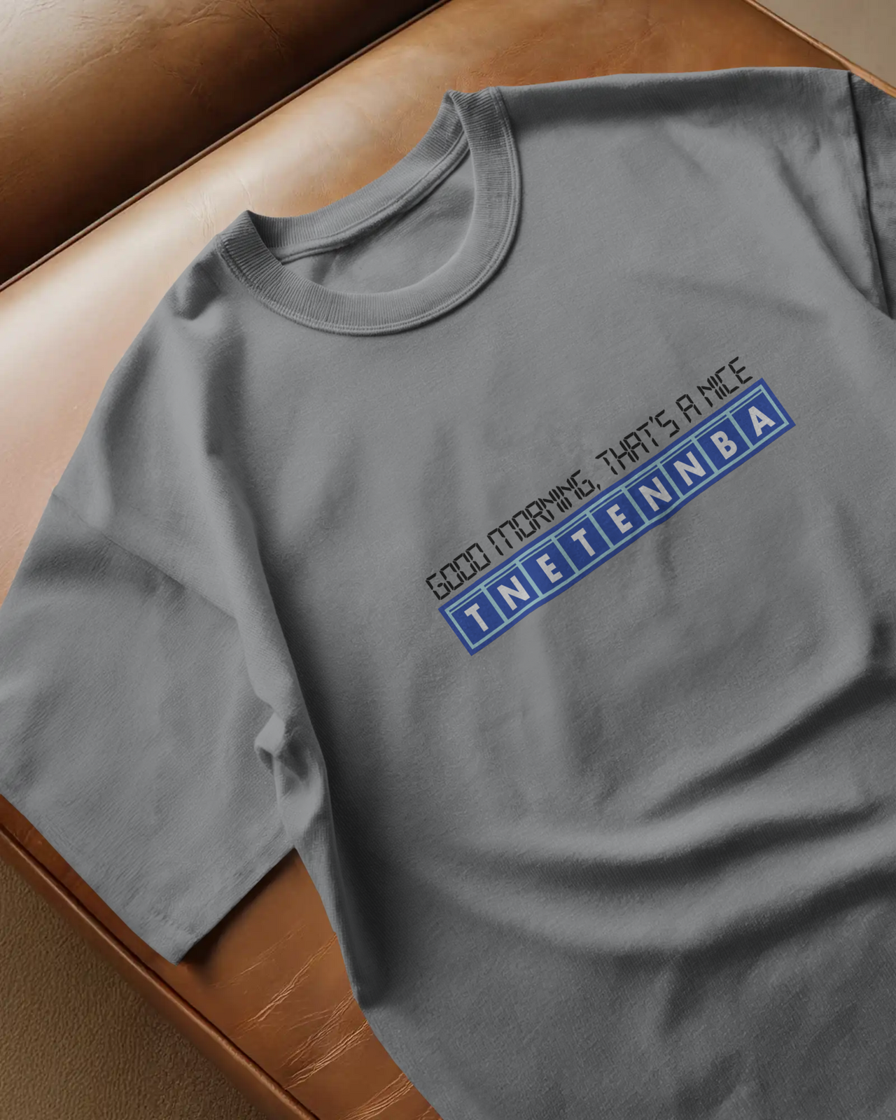 Gray t-shirt with a blue and red logo on a brown surface - IT Crowd - Tnetennba
