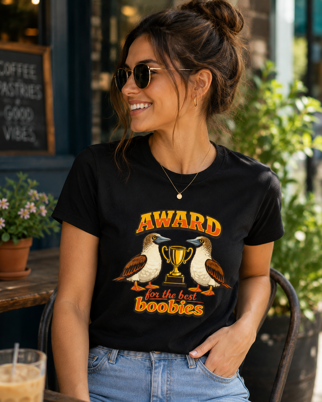 Woman wearing the Award for the Best Boobies T-Shirt in Black while relaxing at an outdoor café.