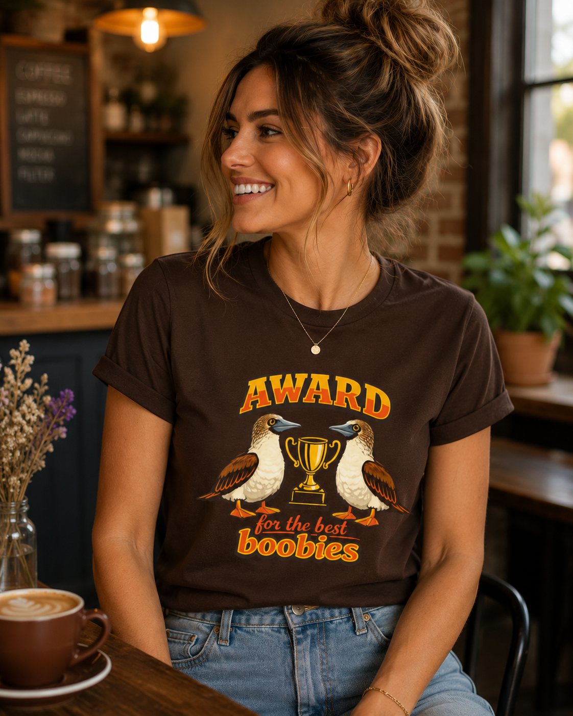 Woman wearing the Award for the Best Boobies T-Shirt in Dark Chocolate inside a cosy rustic coffee shop.