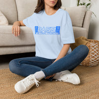 Thumbnail for A woman sitting cross-legged on a woven rug in front of a beige sofa, wearing a light blue oversized T-shirt with a blue graphic that reads 'BASS - THE FINAL FRONTIER' and blue jeans with white sneakers.