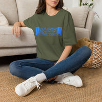 Thumbnail for A woman sitting cross-legged on a woven rug in front of a beige sofa, wearing an olive green t-shirt with a blue graphic that reads 'BASS THE FINAL FRONTIER' and blue jeans with white sneakers.