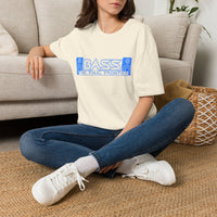 Thumbnail for A woman sitting cross-legged on a woven rug in front of a beige sofa, wearing an oversized cream t-shirt with a blue graphic that reads 'BASS - THE FINAL FRONTIER', blue jeans, and white sneakers.