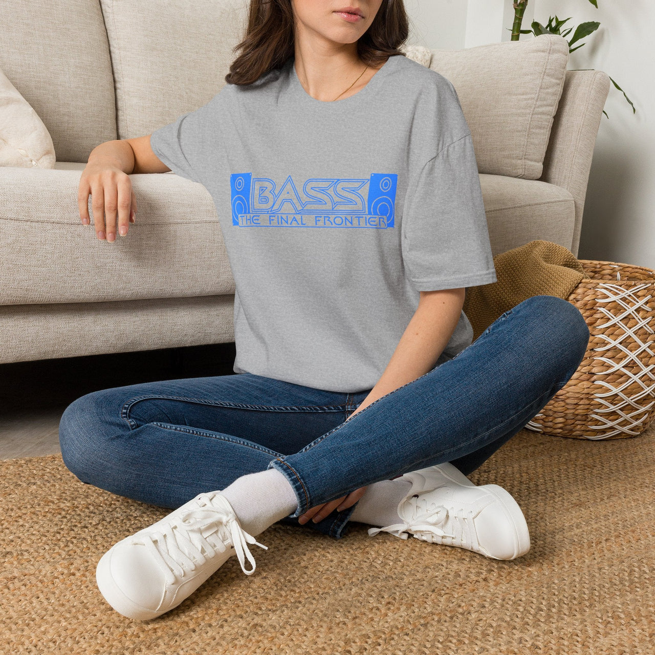 Person sitting on the floor wearing a gray t-shirt with text and blue jeans, in a living room setting.
