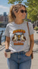 Woman wearing a sport grey Award for the Best Boobies T-shirt outdoors, smiling and drawing attention to the trophy and birds graphic design.