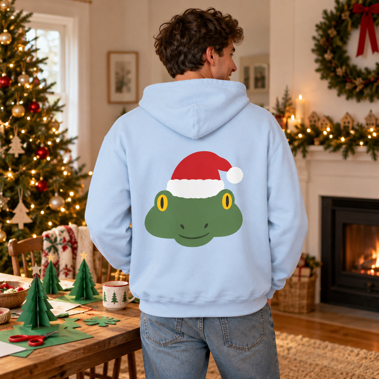 Santa Frog Christmas Back Print Hoodie in Light Blue, worn in a Christmas home setting with the Santa frog back print visible.