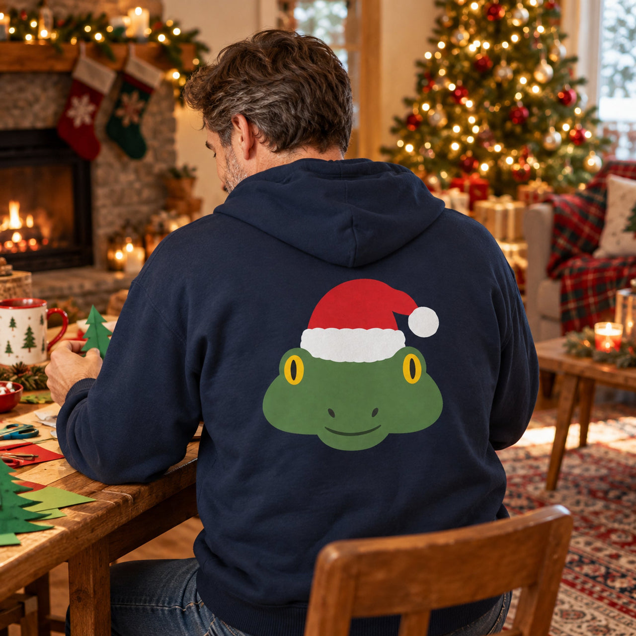 Santa Frog Christmas Back Print Hoodie in Navy, worn in a Christmas home setting with the Santa frog back print visible.