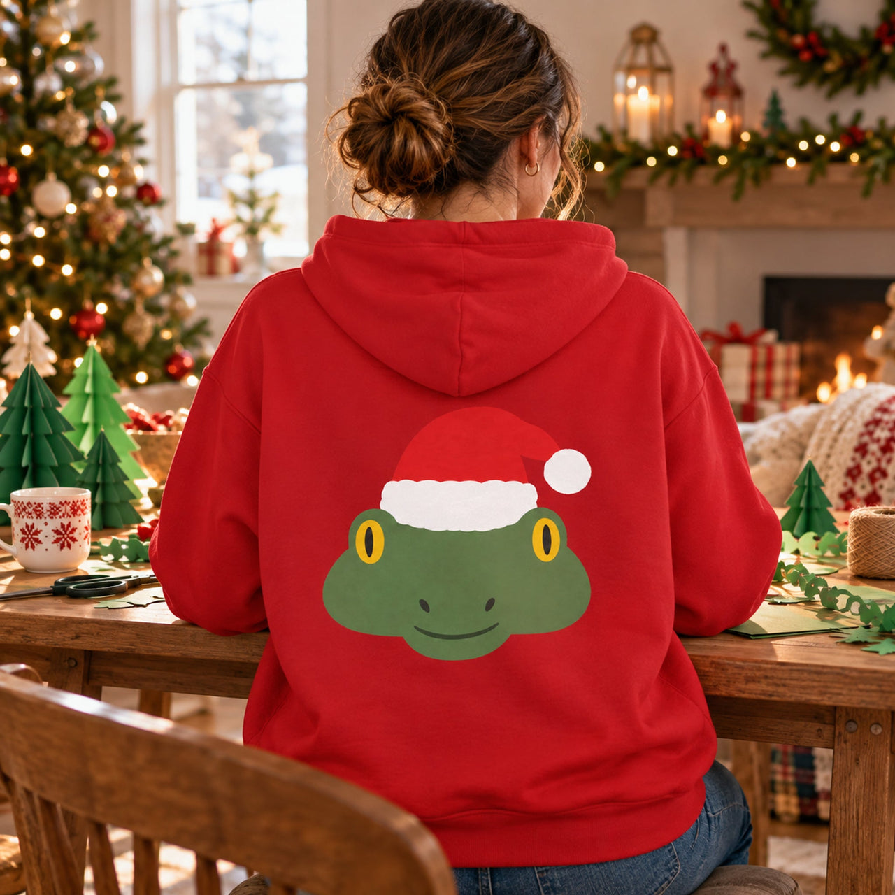 Santa Frog Christmas Back Print Hoodie in Red, worn in a Christmas home setting with the Santa frog back print visible.