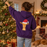 Thumbnail for Santa Giraffe Christmas Back Print Hoodie in Purple, worn in a Christmas home setting with the Santa giraffe back print visible.