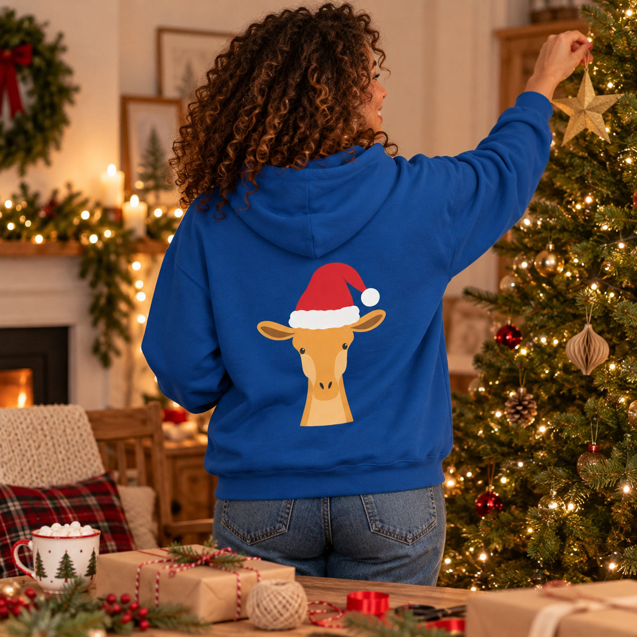 Santa Giraffe Christmas Back Print Hoodie in Royal, worn in a Christmas home setting with the Santa giraffe back print visible.