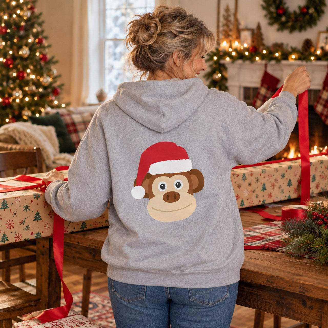 Santa Monkey Christmas Back Print Hoodie in Sport Grey, worn in a Christmas home setting with the Santa monkey back print visible.