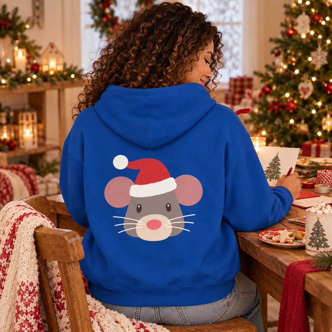 Santa Mouse Christmas Back Print Hoodie in Royal, worn in a Christmas home setting with the Santa mouse back print visible.