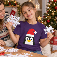 Thumbnail for Santa Penguin Christmas kids t shirt in Purple, worn in a Christmas home setting with the Santa penguin front print visible.
